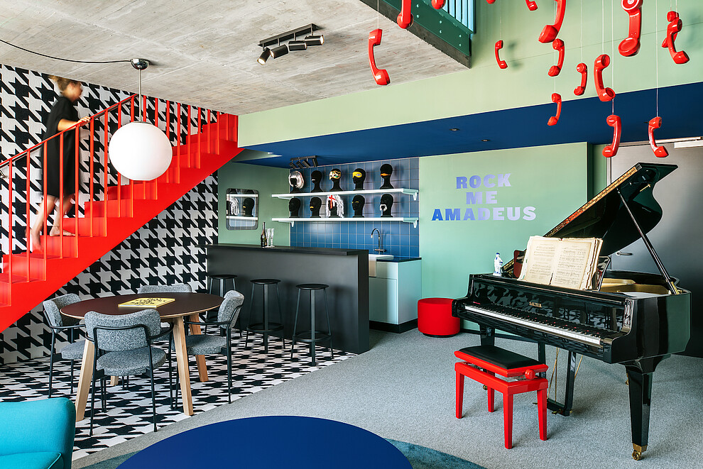 A photo of a Falco-themed living room, featuring a red staircase, a bar area and a grand piano.