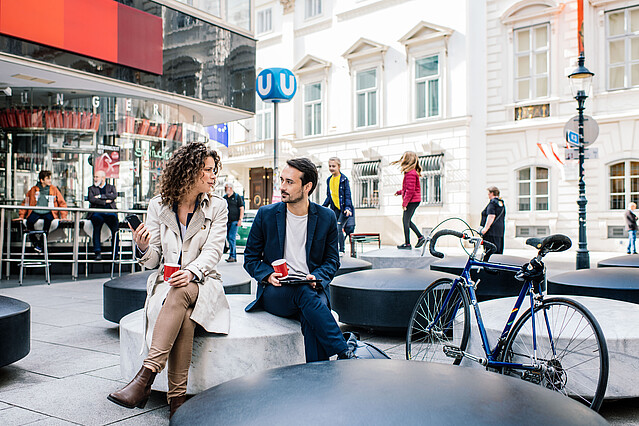 Man and woman sitting on a conrete block in front of a subway station in Vienna